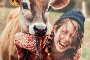 Laughing woman in overalls with a cow's resting head on her shoulder