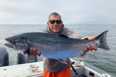Person aboard a fishing boat holding a caught coho salmon