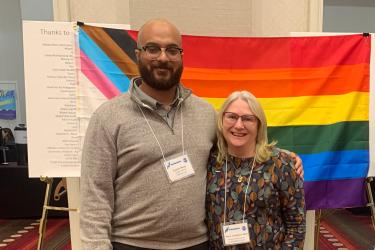 A man (left) and woman (right) stand in front of a pride flag.  Credit: NOAA Fisheries/Lisa Milke