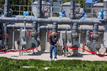 Man stands in front of a large seawater system, cutting red ribbon during a ceremony to celebrate the new upgrade to the system.