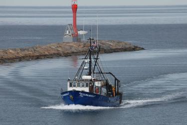 A blue and white vessel with "R/V Gloria Michelle" on each side traverses past a breakwater.