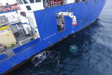 Aerial view of water sampling, crane lowering equipment off the side of the vessel. 