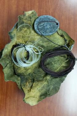 Two coils of fishing line with a hook and lead wight laying on a scrap of fabric on a table. 