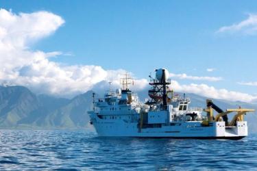 The NOAA ship Oscar Elton Sette on the water with a Hawaiian island in the background. 