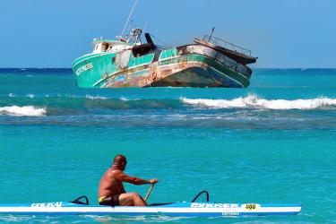 A canoe paddler looks out at the ground vessel Pacific Paradise.