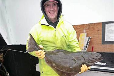 Scientist in yellow coat holding a large brown fish