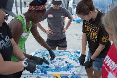 People with gloves and nametags sort pieces of marine plastic onto a NOAA template on a table. 