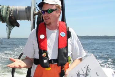 John Rosendale at the stern of Navoo with pfd and chart.