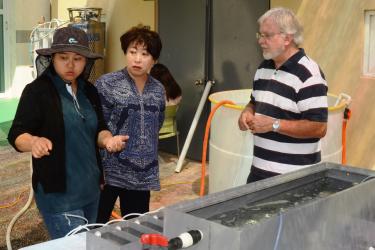 Scientist discussing experiments, silver tank in foreground.