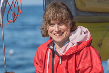 Portrait of brunette woman with orange coat on a boat with ocean in background. 