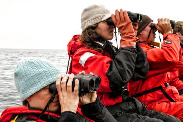 People in orange suits looking through binoculars on a boat