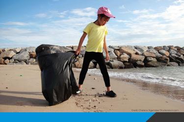 Kid on a beach carrying a garbage bag to collect trash