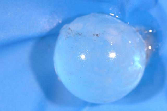 Photograph of a shiny translucent spherical eye lens on a light blue background