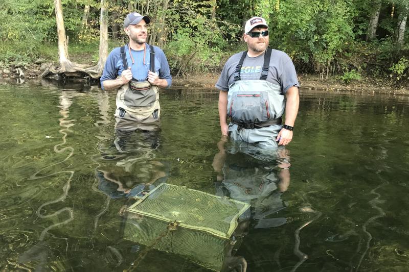 Two scientists stand in a stream, next to water quality testing equipment under the surface.