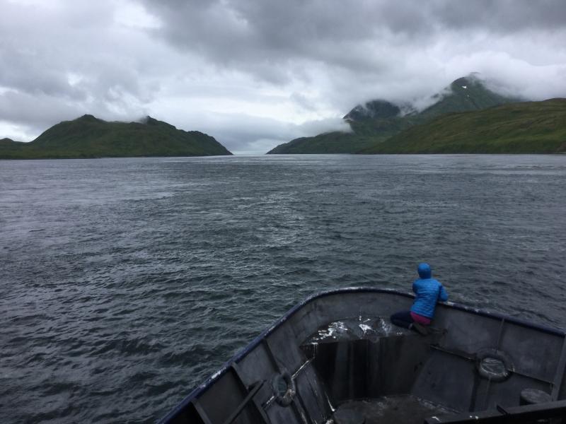 Photo of person sitting in the bow of a boat looking towards a strait.