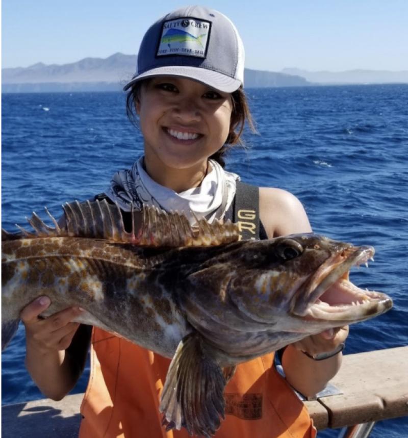 Young female scientist on a survey vessel smiling and holding a large groundfish