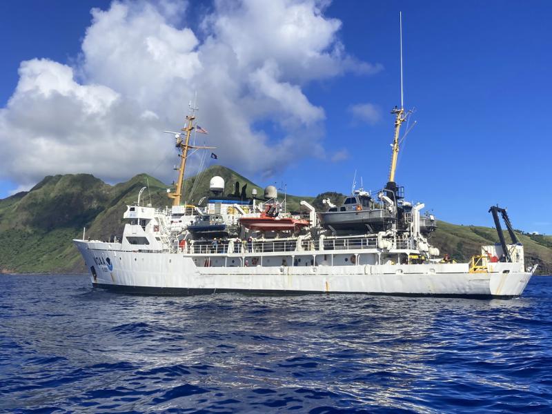 NOAA ship Rainier floats with an island in the background.
