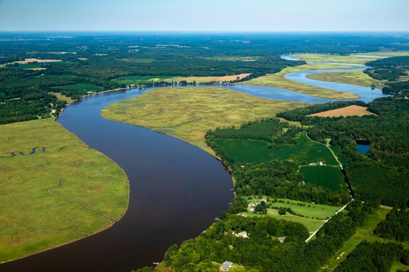 A river meanders past residential areas, marshes, forests, and agricultural operations.