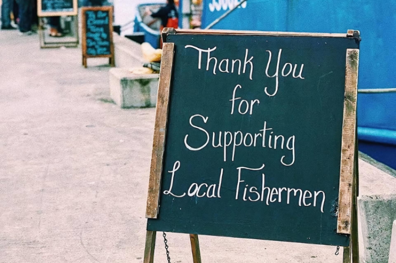 A chalk signboard outside a fish market that says "Thank You for Supporting Local Fishermen"