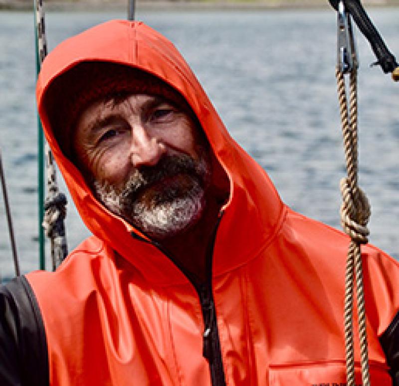 Portrait of scientist wearing an orange jumpsuit with the ocean in the background.