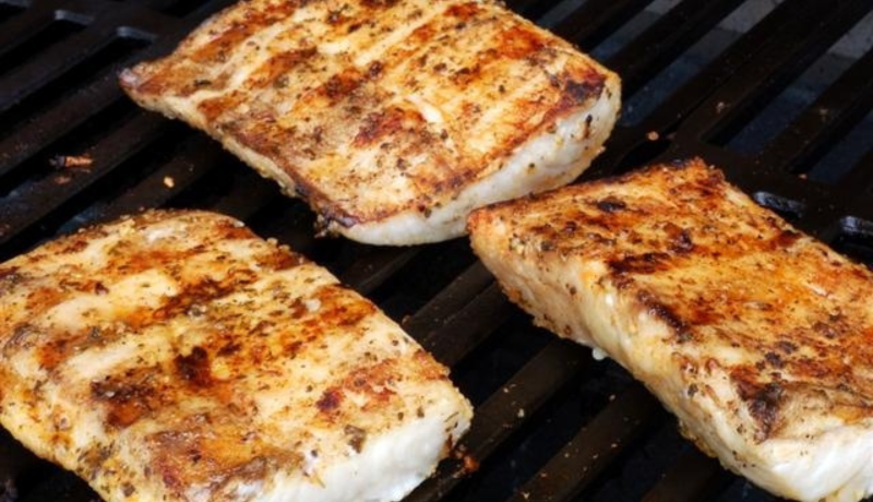 Four rectangular white fish steaks on a black grill with browned grill marks on the meat.