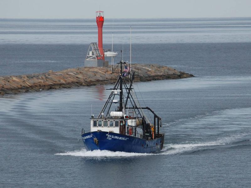 A blue and white vessel with "R/V Gloria Michelle" on each side traverses past a breakwater.