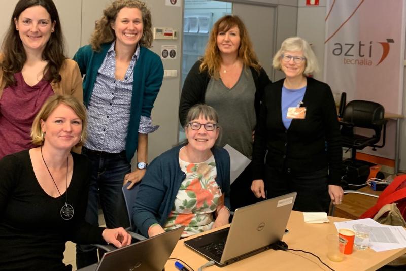 Trish Clay sitting at desk with five women standing around her.