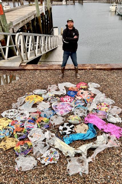 A fisherman standing behind a circle of 50 deflated Mylar balloons that he collected from the ocean.