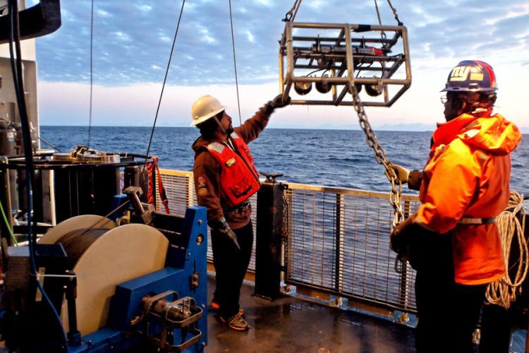 Photo of two people using a winch to lower the stereo camera system into the ocean from the deck of a ship in Alaska