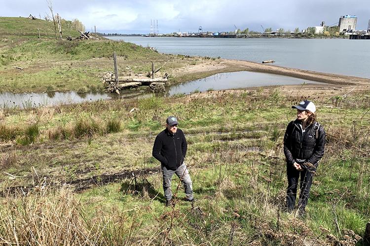 Two people stand on a grassy hill near a river