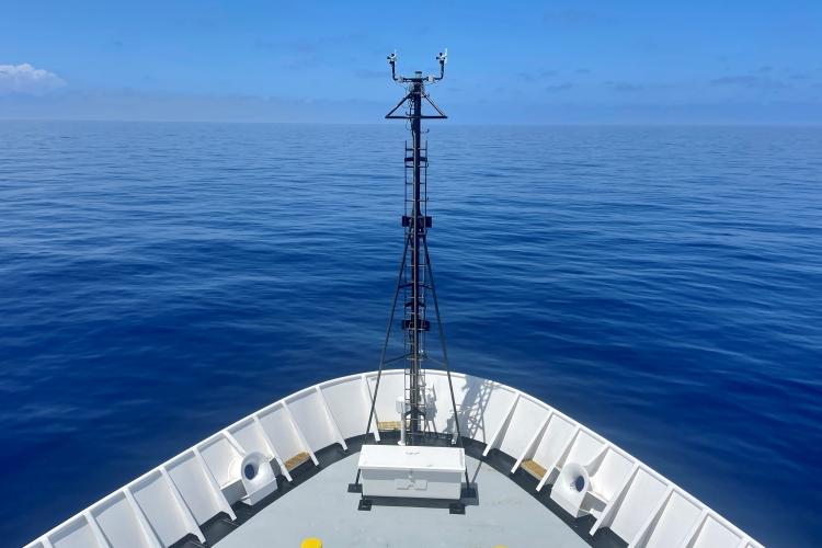 The bow of a large white ship in an open ocean of blue water.