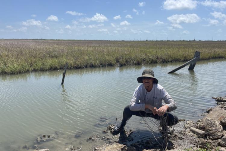 A woman crouching and smiling on a muddy oyster bank