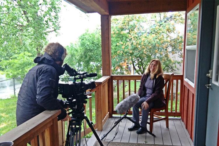 Person pointing a camera at a scientists on a porch