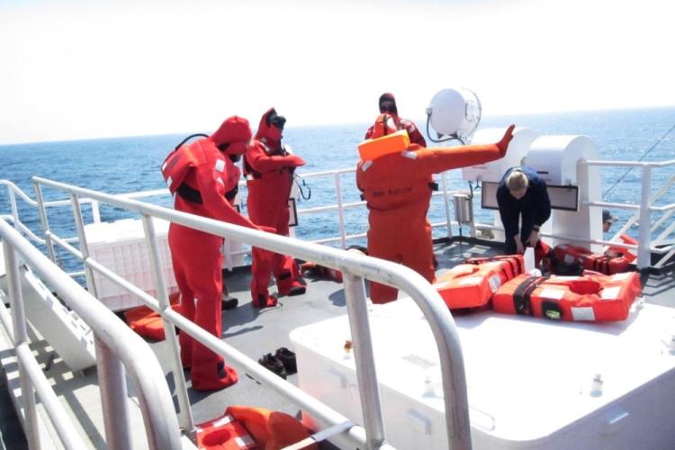 Staff learning how to don immersion suits, bright orange safety gear.