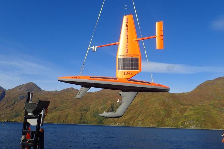 Orange sail drone being lifted out of the ocean with green hills in background. 