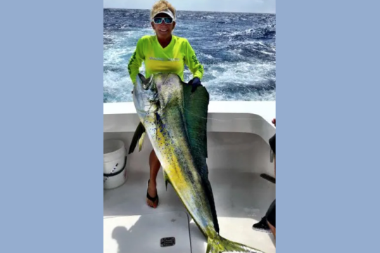 Woman holds caught mahi mahi aboard boat with water in the background