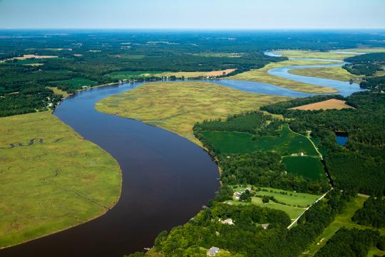 Aerial view of river with wetlands interspersed with residences and forested areas on both sides