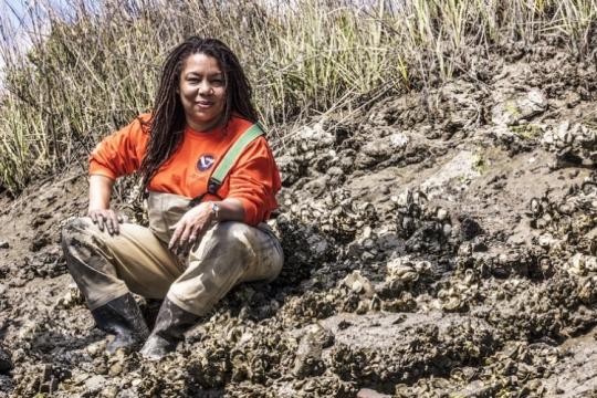 Dr. Dionne Hoskins-Brown sitting next to an oyster reef. 