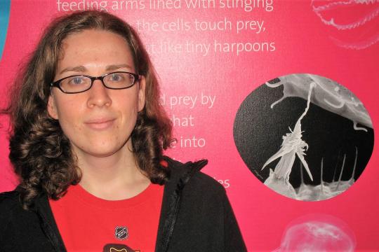 A woman poses in front of a poster featuring a black and white image of a nematocyst.