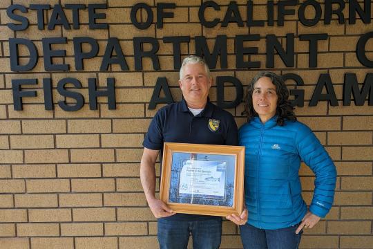  Matt Johnson and Jennifer Quan standing in front of a brick wall with signage that says "California Department of Fish and Wildlife"