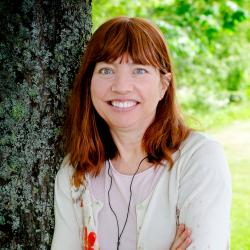 Photo of Maggie Mooney-Seus with tree trunk and green space in the background.