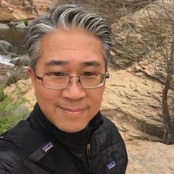 Selfie photo of Jim Lee with high desert rocks and mountain stream in the background.