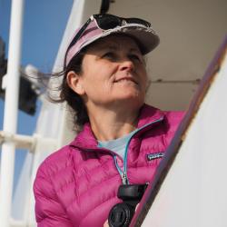 Photograph of Shannon Rankin at sea - she is holding a camera, getting ready to photograph marine mammals.