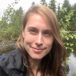 Female scientist stands in front of a wetland with trees and leaves in the background