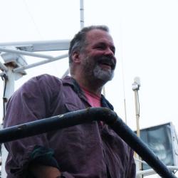 Ned Laman stands on a boat under and overcast sky