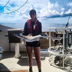 Kendell on a boat holding a fish. 