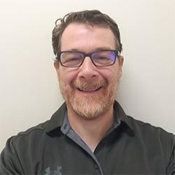 Portrait of man with glasses smiling with grey polo against a white wall background