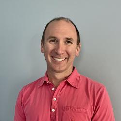 Smiling male scientist with brown hair wearing coral shirt