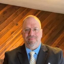 Michael Stratton, bearded gentleman in blue shirt, checkered tye and brown jacket. 