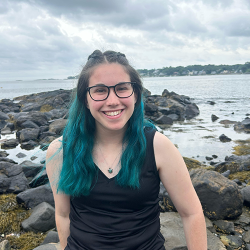 Smiling women with glasses and long hair on a rocky beach.